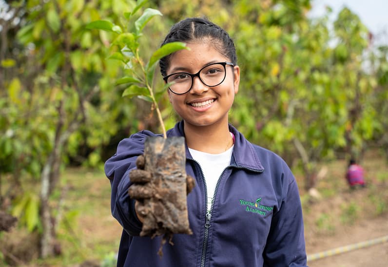 A female Young Living Academy student holds a tree sapling.