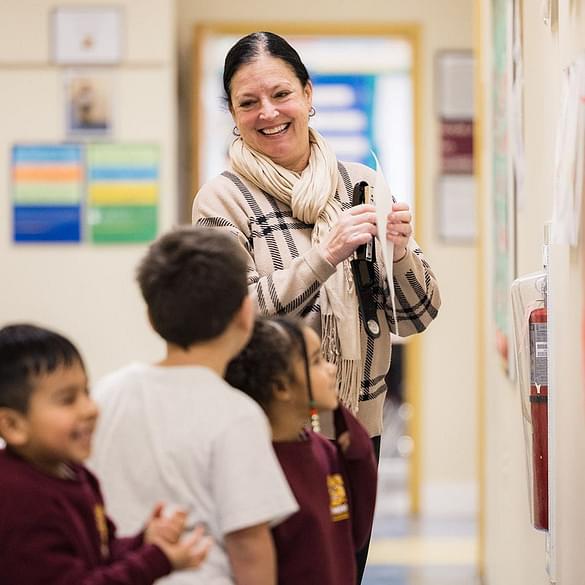 Teacher smiles at young students in hallway