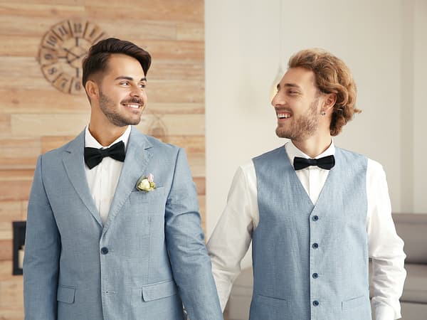 gay couple holding hands and smiling at each other after getting married online.