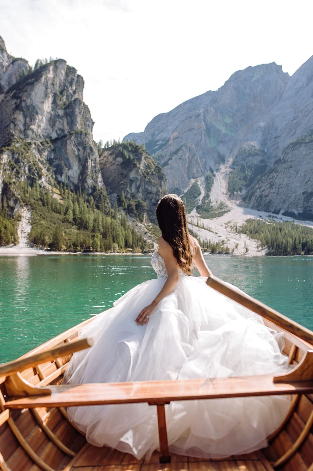 Bride stands at the bow of a boat going across a lake