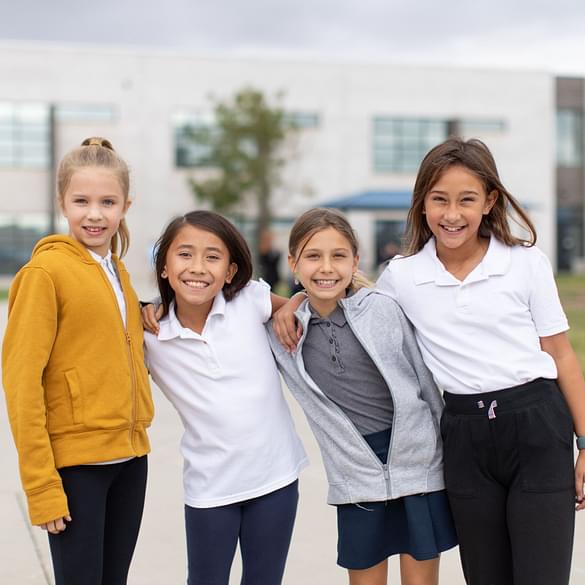  Female elementary student smiling at desk with hands clasped together. 