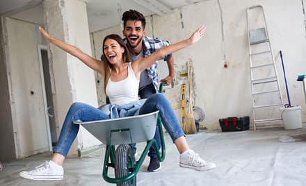 husband enjoying life with wife while pushing her in a wheelbarrow in a house under construction