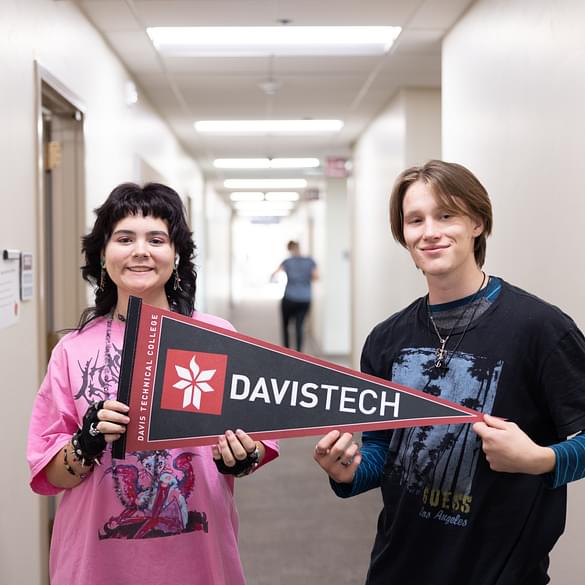 Two smiling students, a girl in a pink top and a boy in a dark t-shirt, holding a 'DAVISTECH' pennant. This image highlights Career Path High's strong partnership with Davis Technical College , offering dual enrollment opportunities and a clear pathway for students to gain foundational career skills.