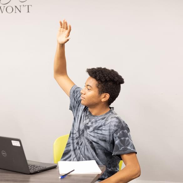 A student raising his hand while working on a laptop, symbolizing Career Path High's adaptive learning environment and personalized support for every student to succeed